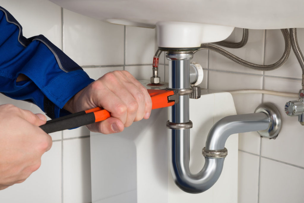 a plumbers using a wrench to fix a pipe under a sink / scott hart