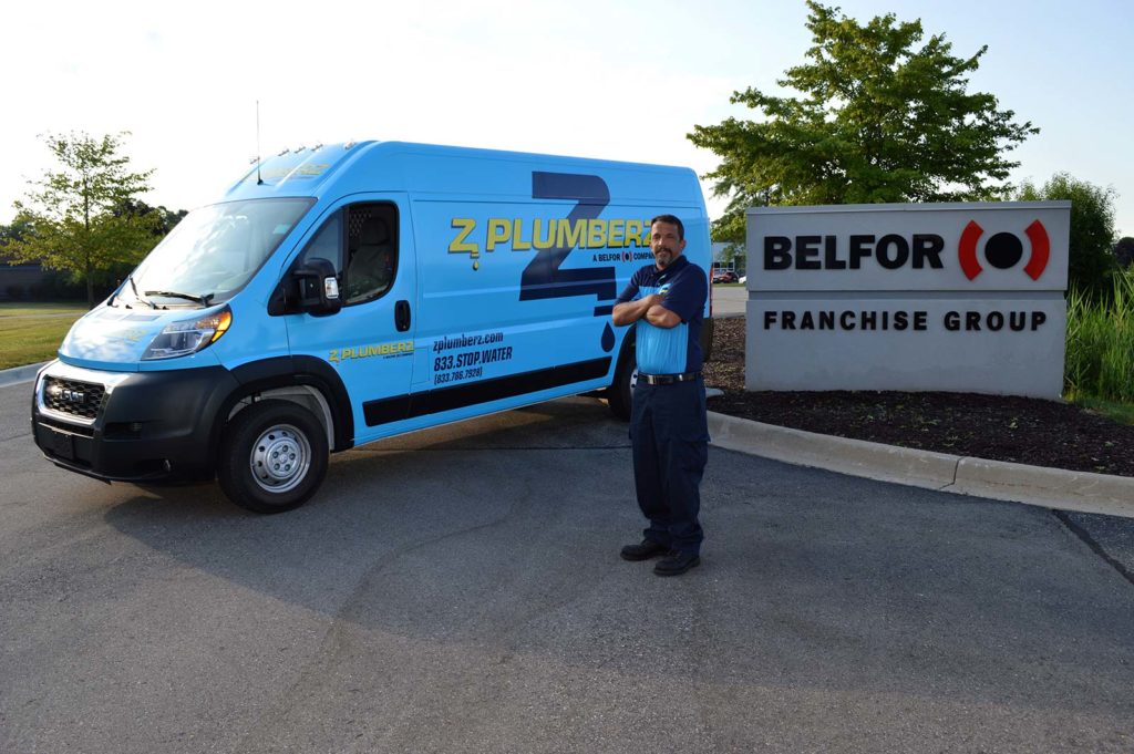 Z PLUMBERZ plumbing franchise opportunity franchisee stands in front of the Z PLUMBERZ van and BELFOR Franchise Group sign